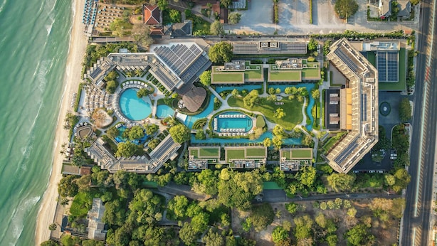 Een vogelperspectief van een resort met meerdere zwembaden, een strand en een weg parallel aan het water.