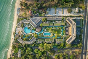 Een vogelperspectief van een resort met meerdere zwembaden, een strand en een weg parallel aan het water.
