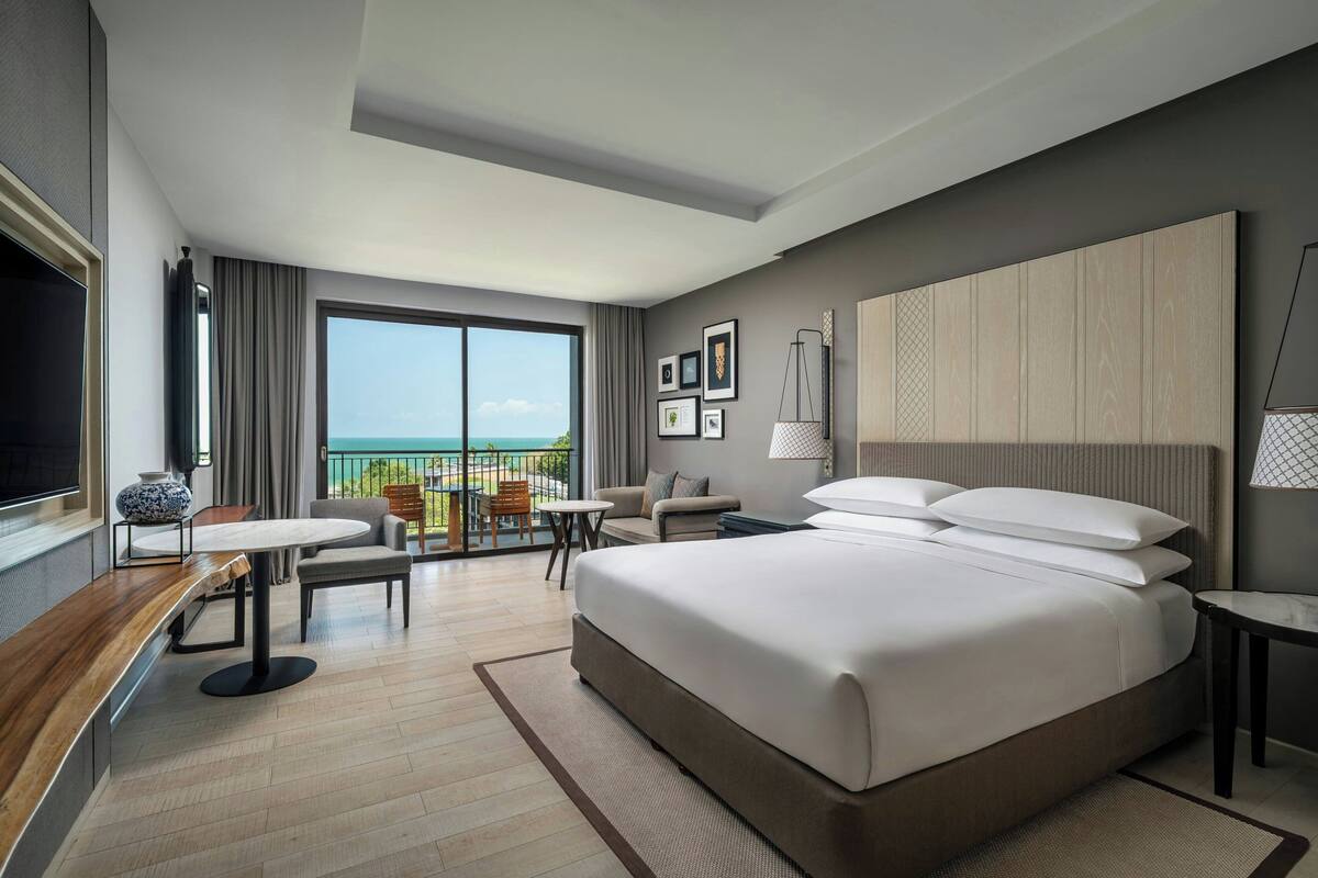 Een moderne hotelkamer met een groot bed, een zithoek, een televisie en een balkon met uitzicht.