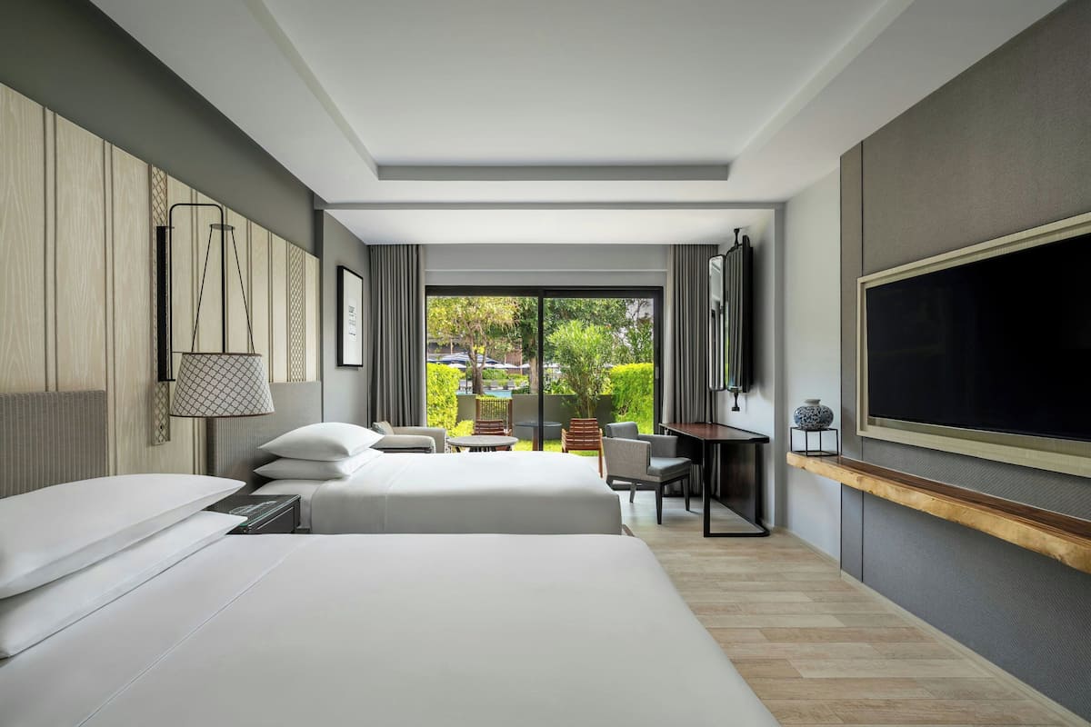 Een hotelkamer met twee bedden, een televisie, een bureau en uitzicht op groen.