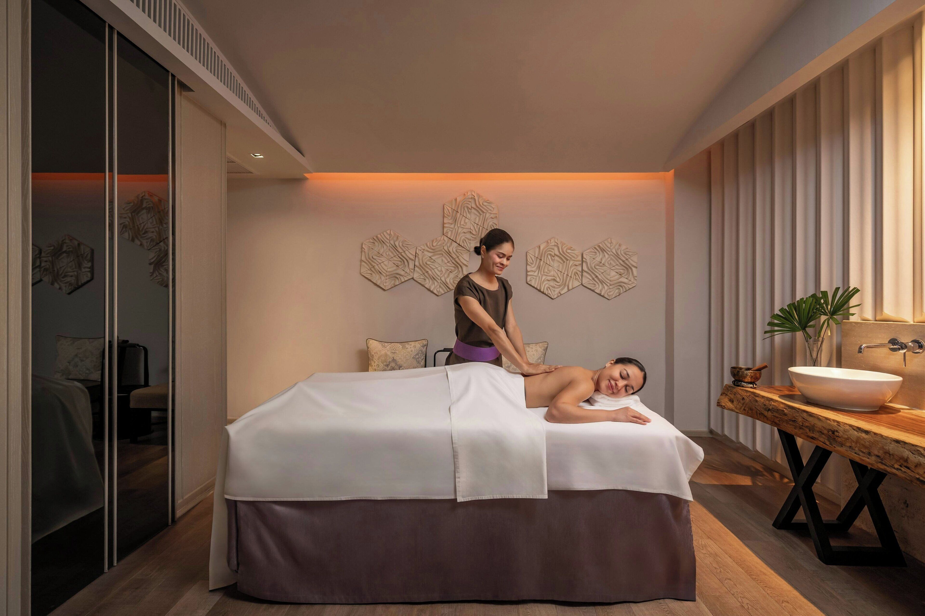 A massage room with a massage table, a person receiving a massage, and a wooden side table with a bowl.