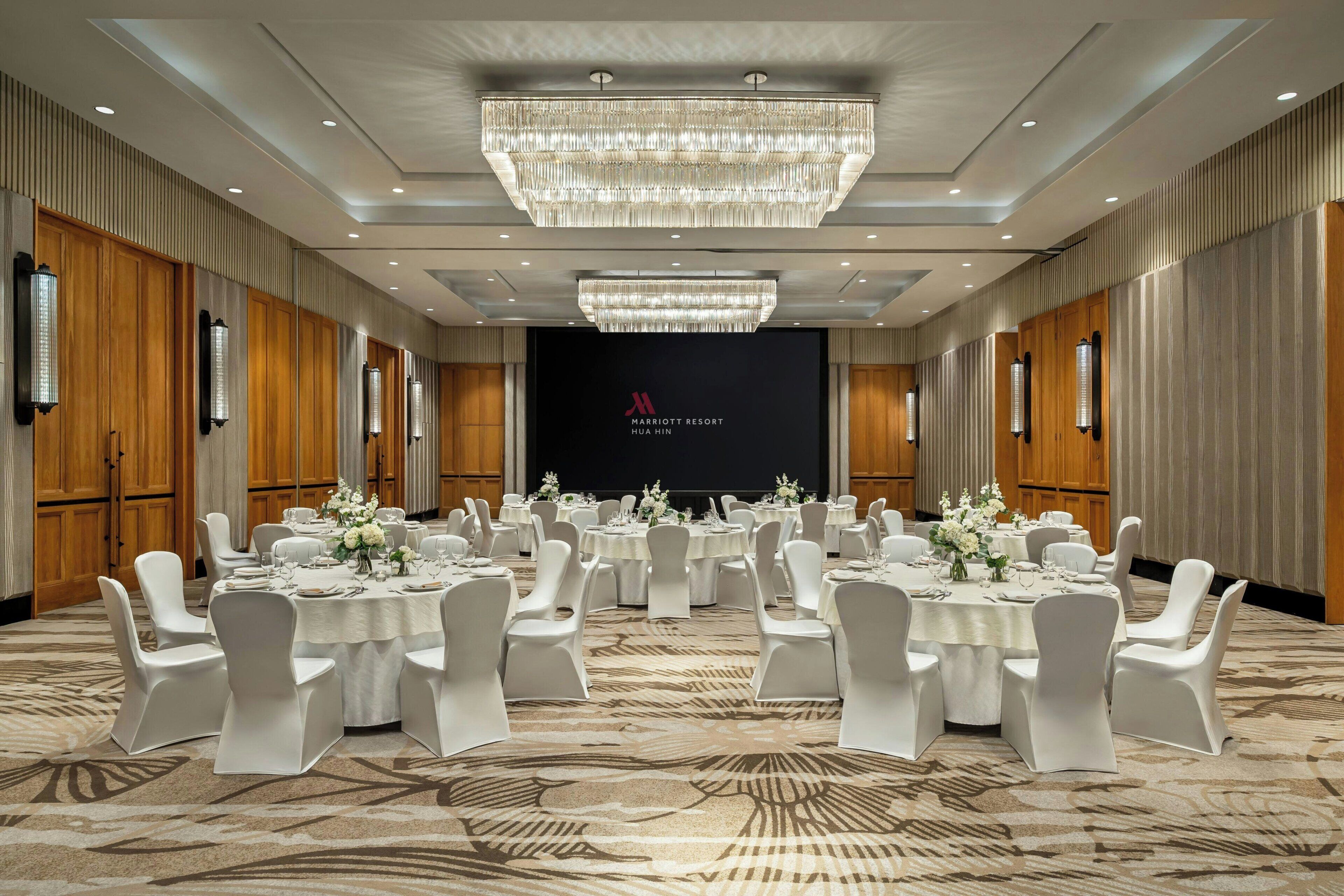 Un salón de conferencias con mesas redondas, sillas blancas y una gran lámpara de cristal.