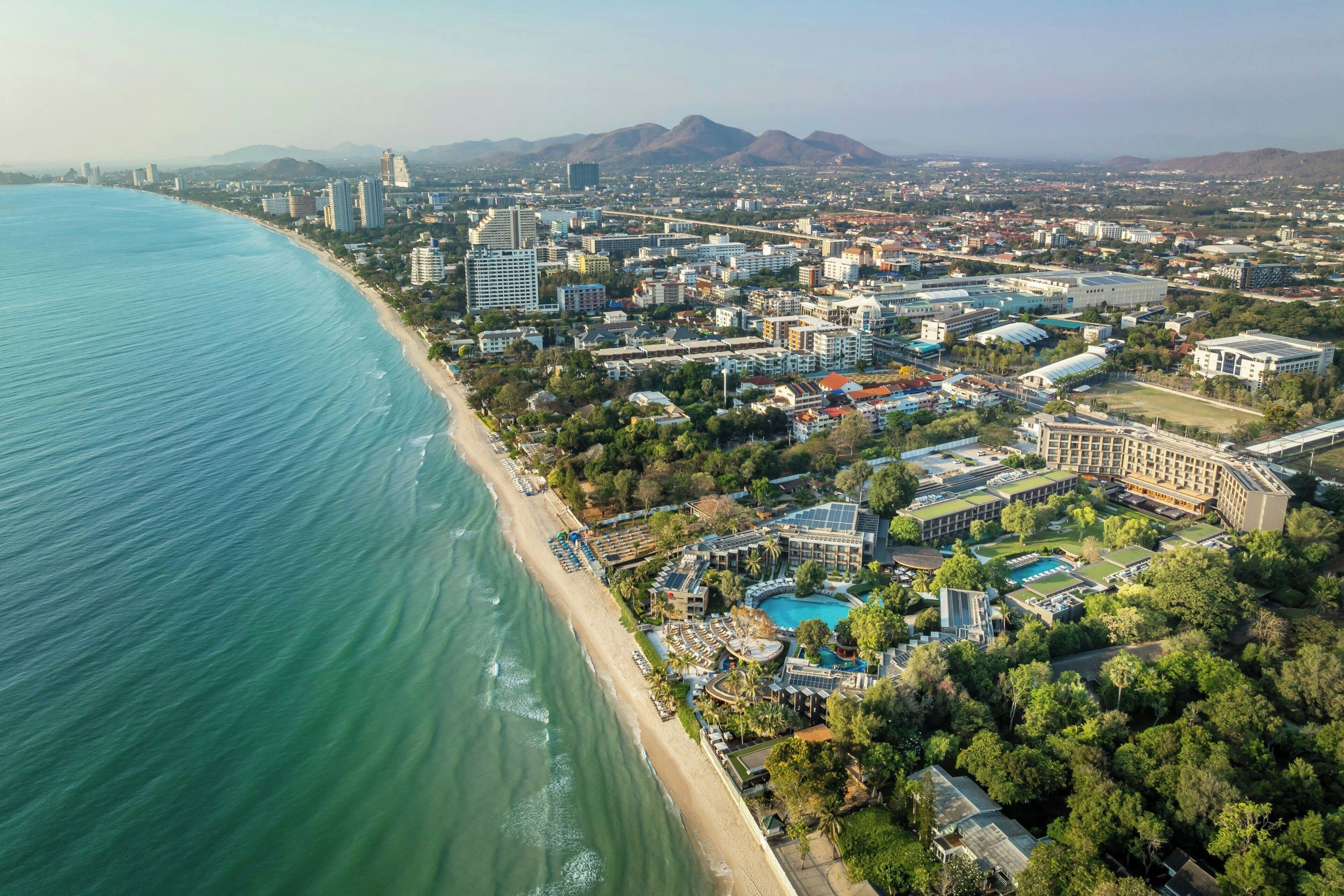 Vue aérienne d’une ville côtière avec une plage, un hôtel et les bâtiments environnants.