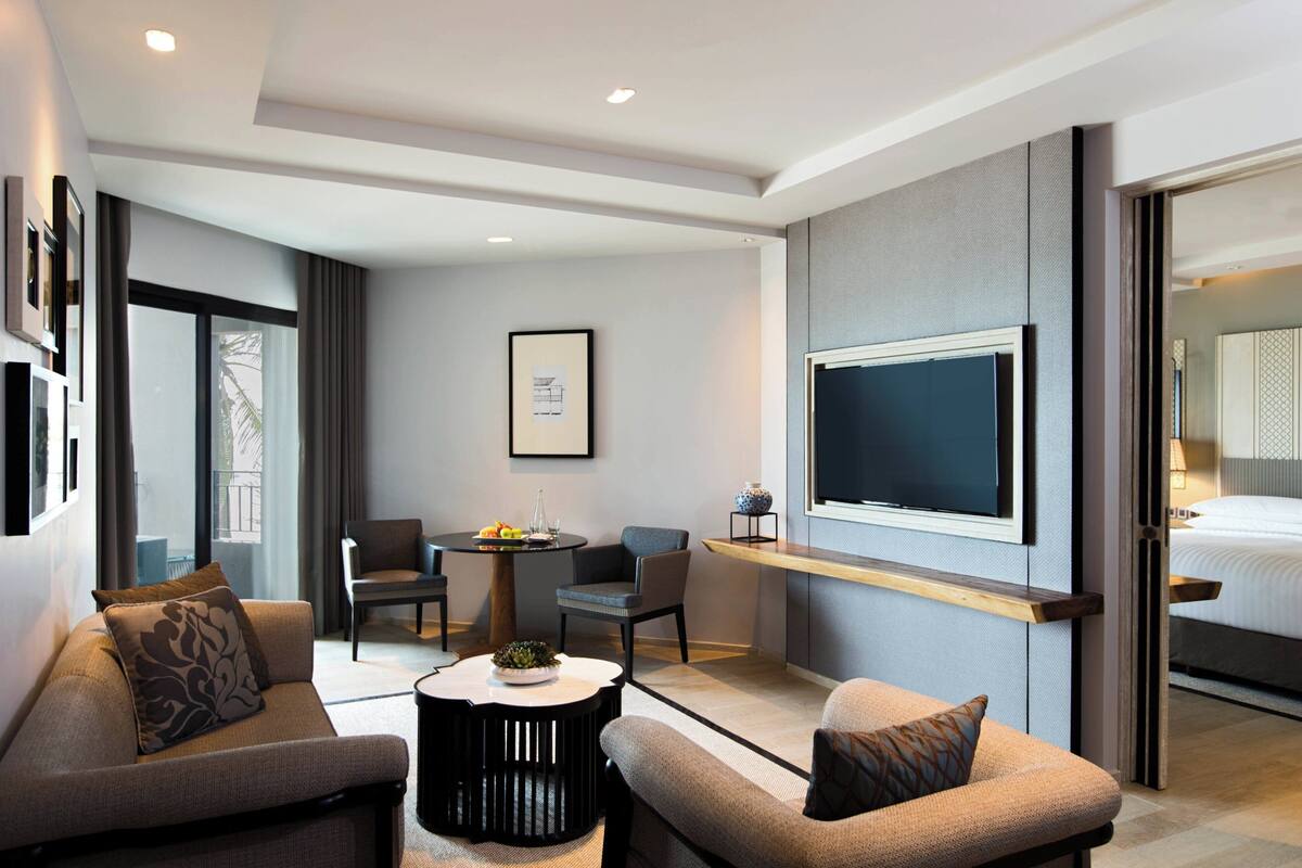 Een moderne hotelkamer met een bank, fauteuils, een salontafel, een televisie en een bed.