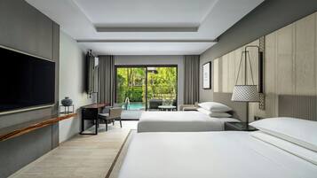 A modern hotel room with a large bed, a desk, a chair, a TV, and a view of a pool and greenery.