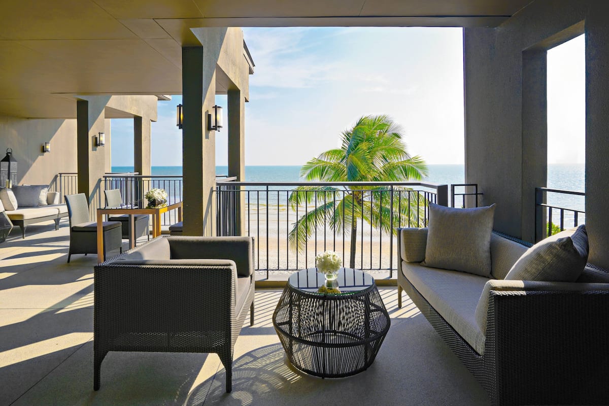 A balcony with wicker furniture, a round table, and a view of the ocean.