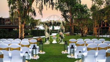 Montaje para una ceremonia de boda con sillas blancas, adornos florales y faroles.