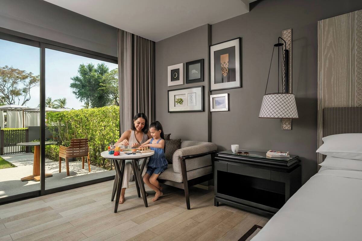 Een moderne hotelkamer met een groot raam, een eettafel, een bank, een tv-meubel en ingelijste foto's aan de muur.