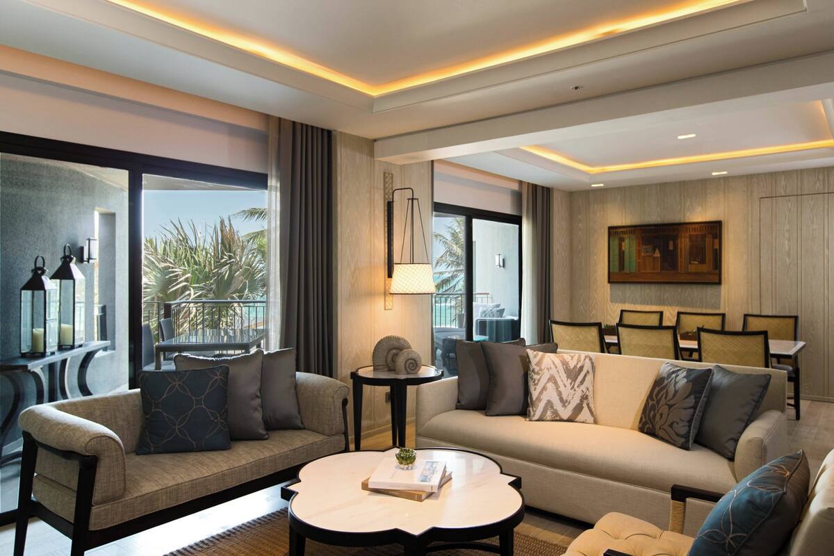 Een moderne hotelkamer met een bank, fauteuils, een ronde salontafel en een eethoek met stoelen en een tafel.