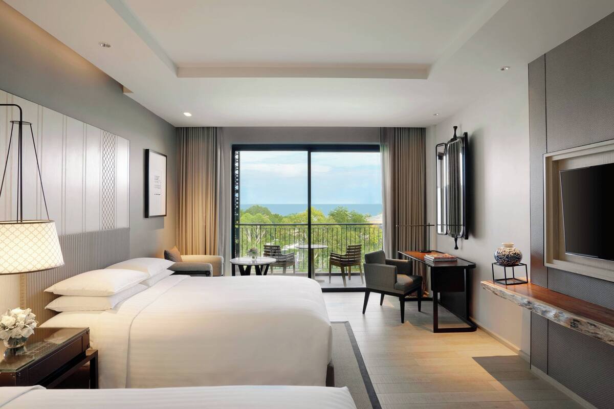 Hotelkamer met twee bedden, een bureau, een televisie en een balkon met uitzicht op zee.