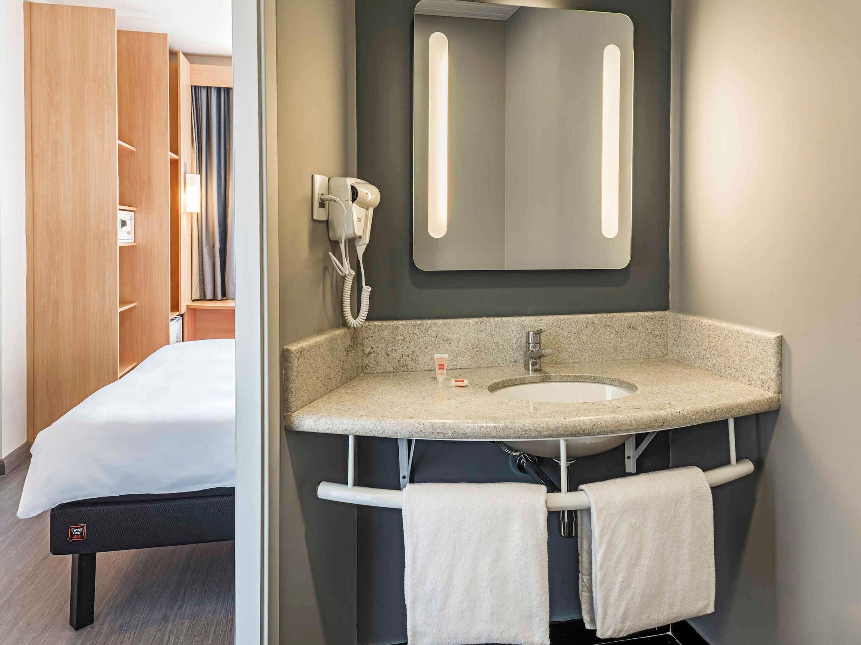 A hotel room with a bed, a bathroom with a sink, a mirror, and a hairdryer.