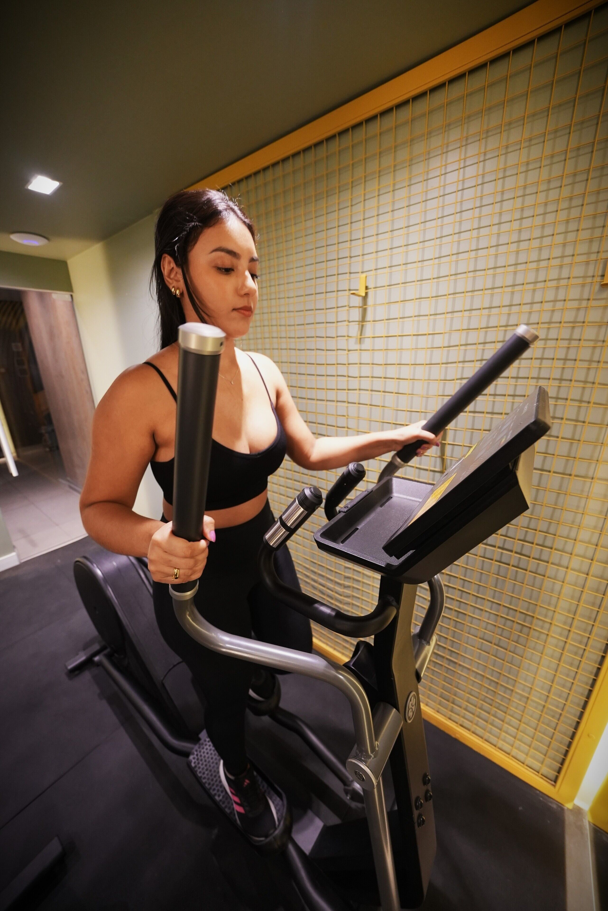 A person using an elliptical machine in a gym with a tiled wall and a door in the background.