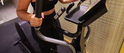 A person using an elliptical machine in a gym with a tiled wall and a door in the background.