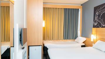 Quarto de hotel com duas camas, televisão, mini-frigorífico e uma janela grande com cortinas.