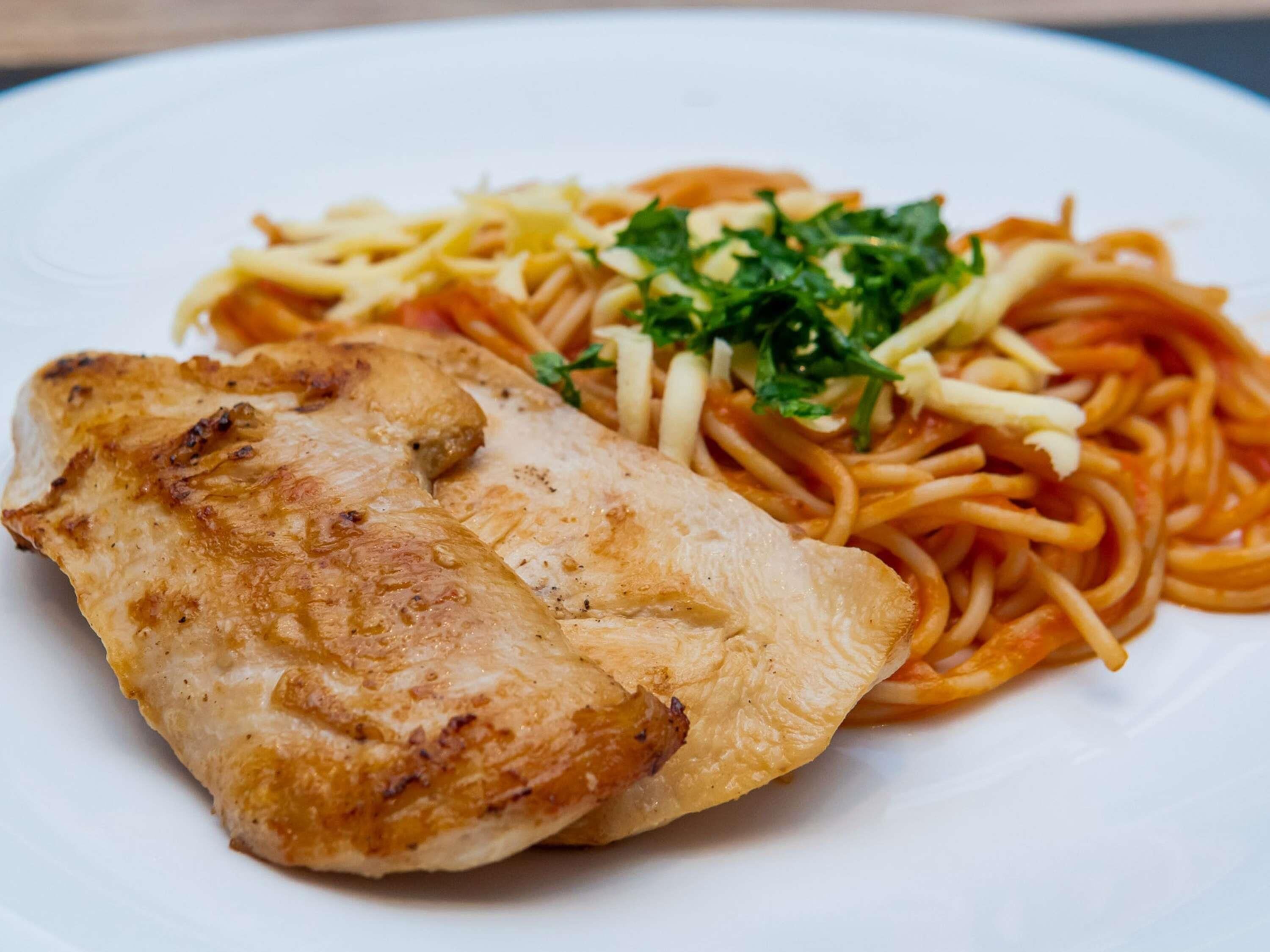 Une assiette contenant un morceau de poulet grillé et des spaghettis, le tout agrémenté d’une garniture.