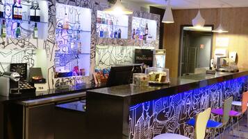 A bar area with a counter, shelves of beverages, and a wall with abstract art.