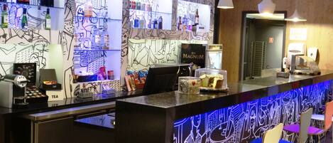 A bar area with a counter, shelves of beverages, and a wall with abstract art.