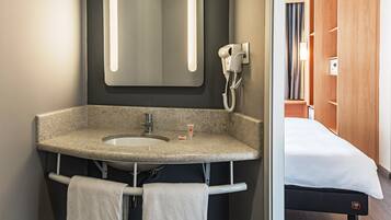 Un baño moderno con lavamanos de granito, un espejo, un secador de pelo y un perchero para toallas.