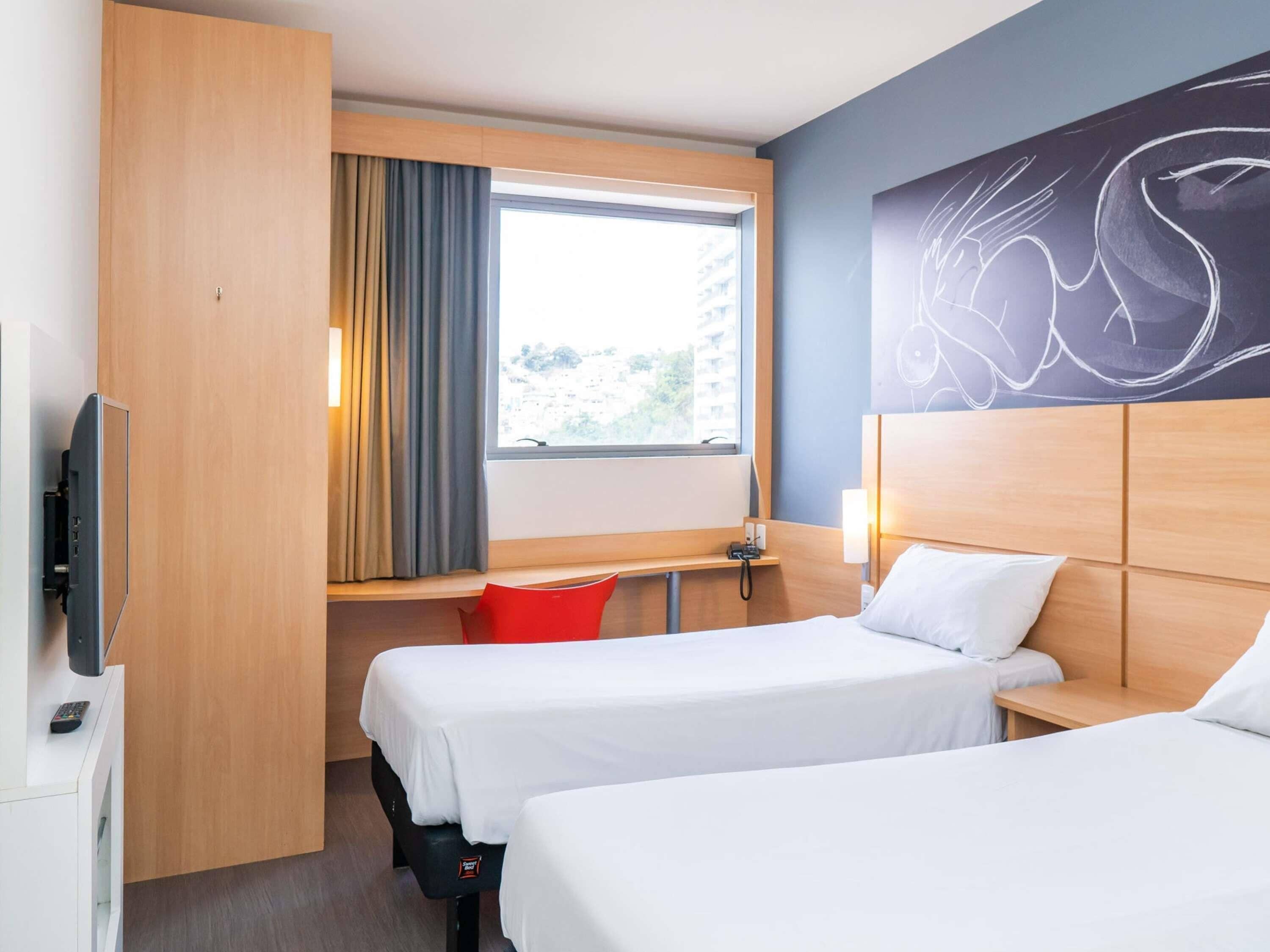 Een hotelkamer met twee bedden, een bureau, een stoel, een televisie en een raam met gordijnen.