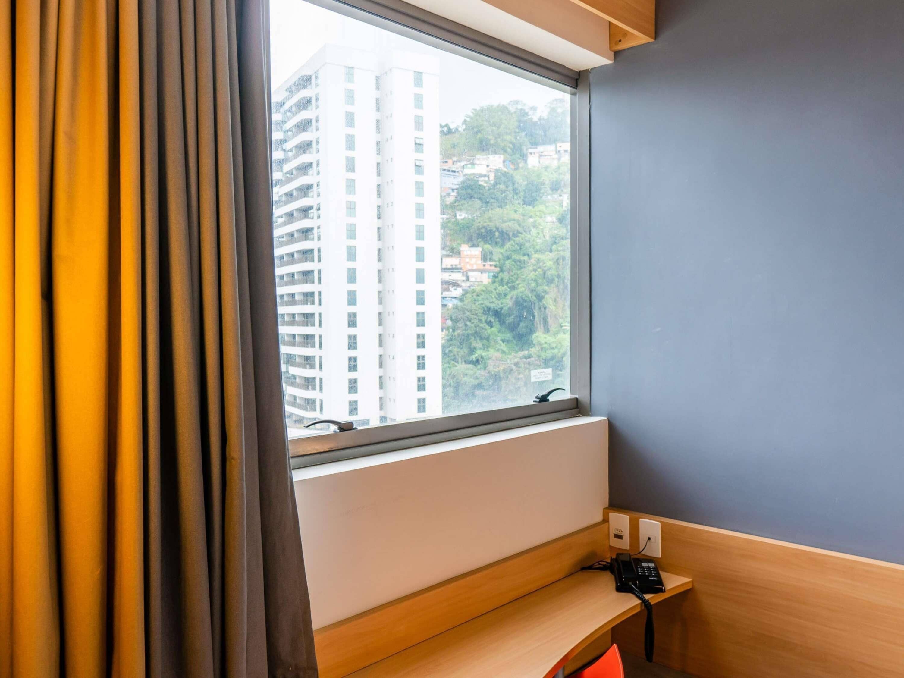 A hotel room with a window, a desk, and a telephone.