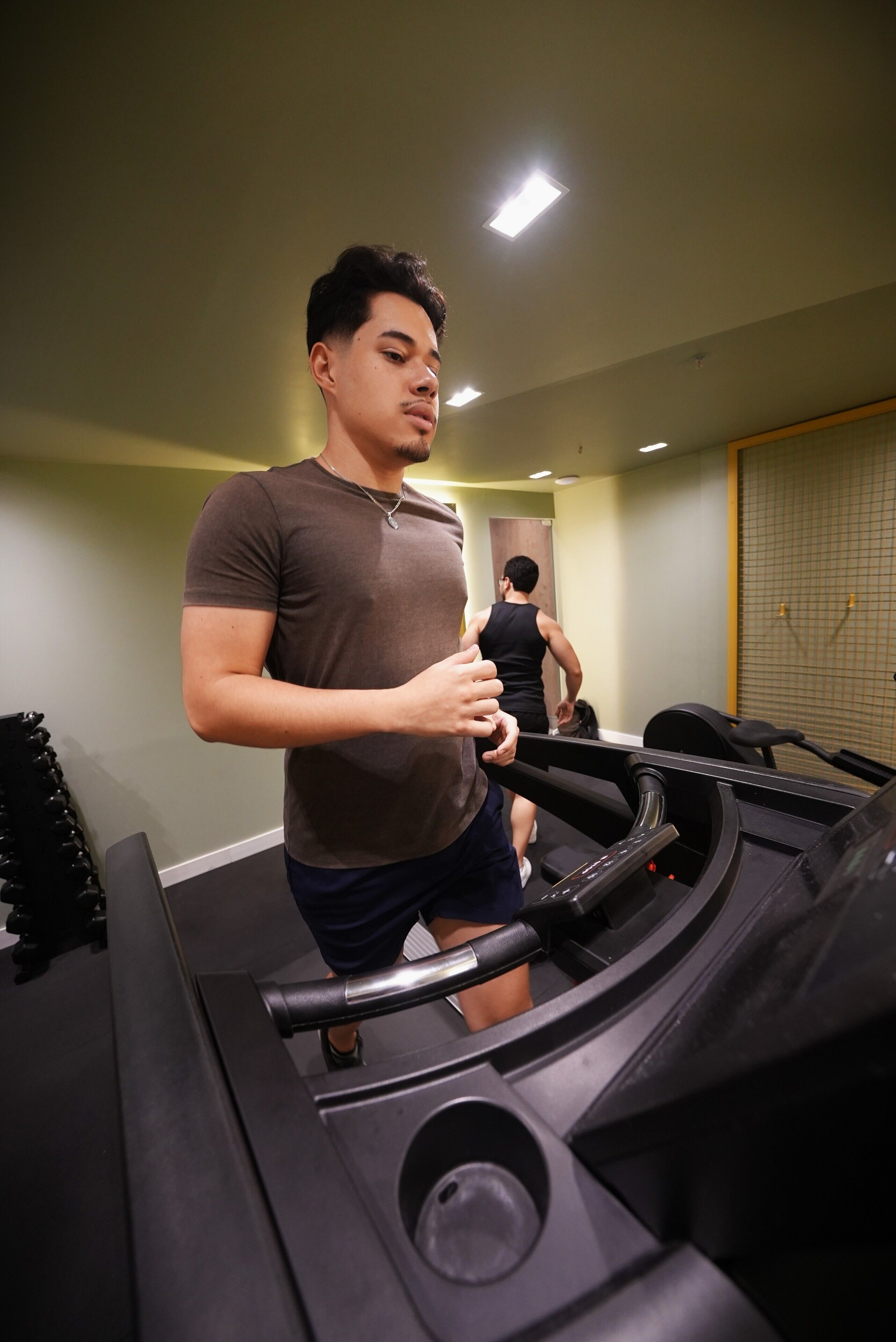 A gym with treadmills, a person using a treadmill, and another person walking in the background.