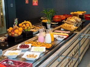 Un bufé con diversas opciones de comida, incluyendo frutas, quesos y panes.