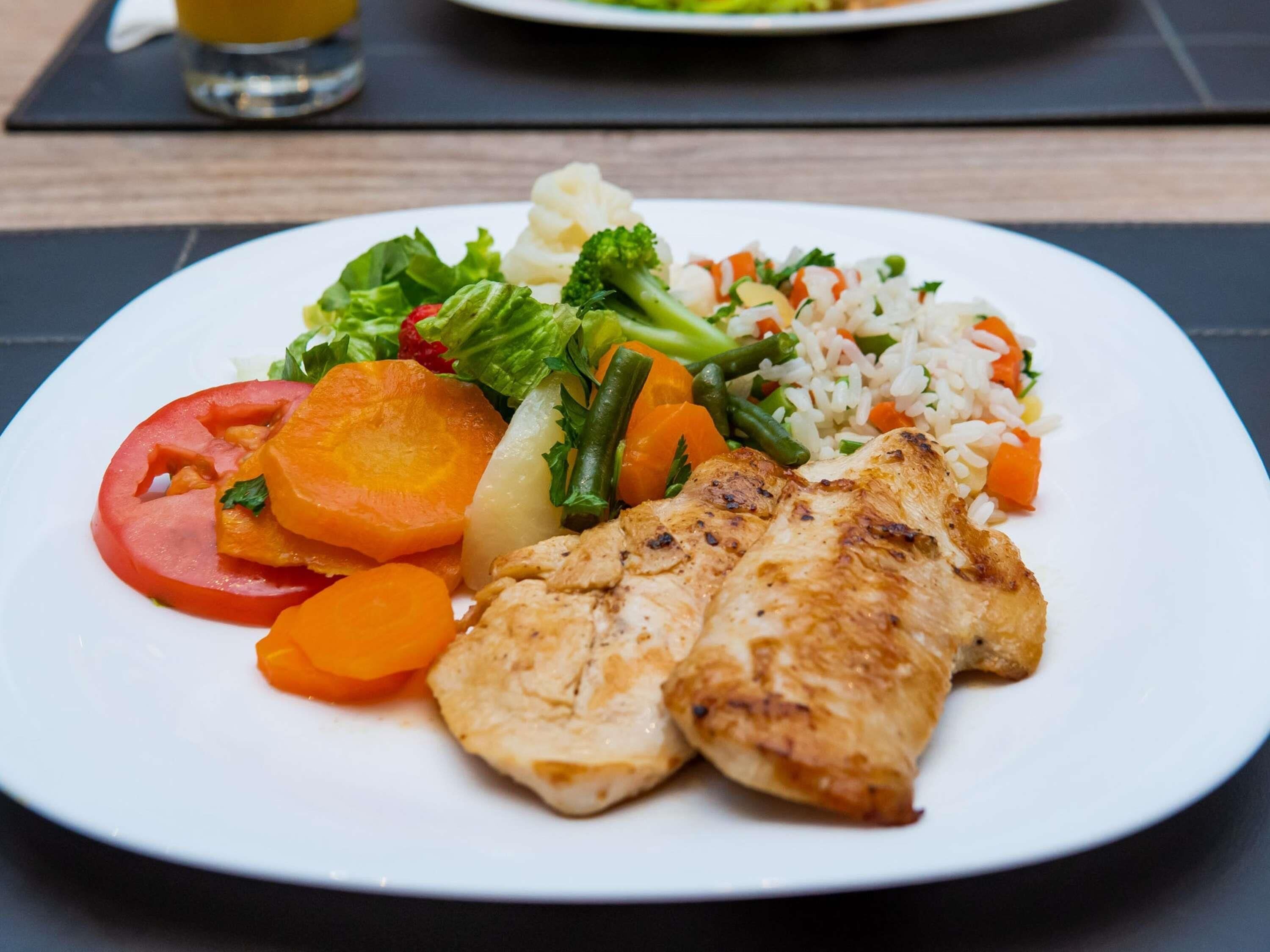 Une assiette composée de poulet grillé, de légumes et de riz.