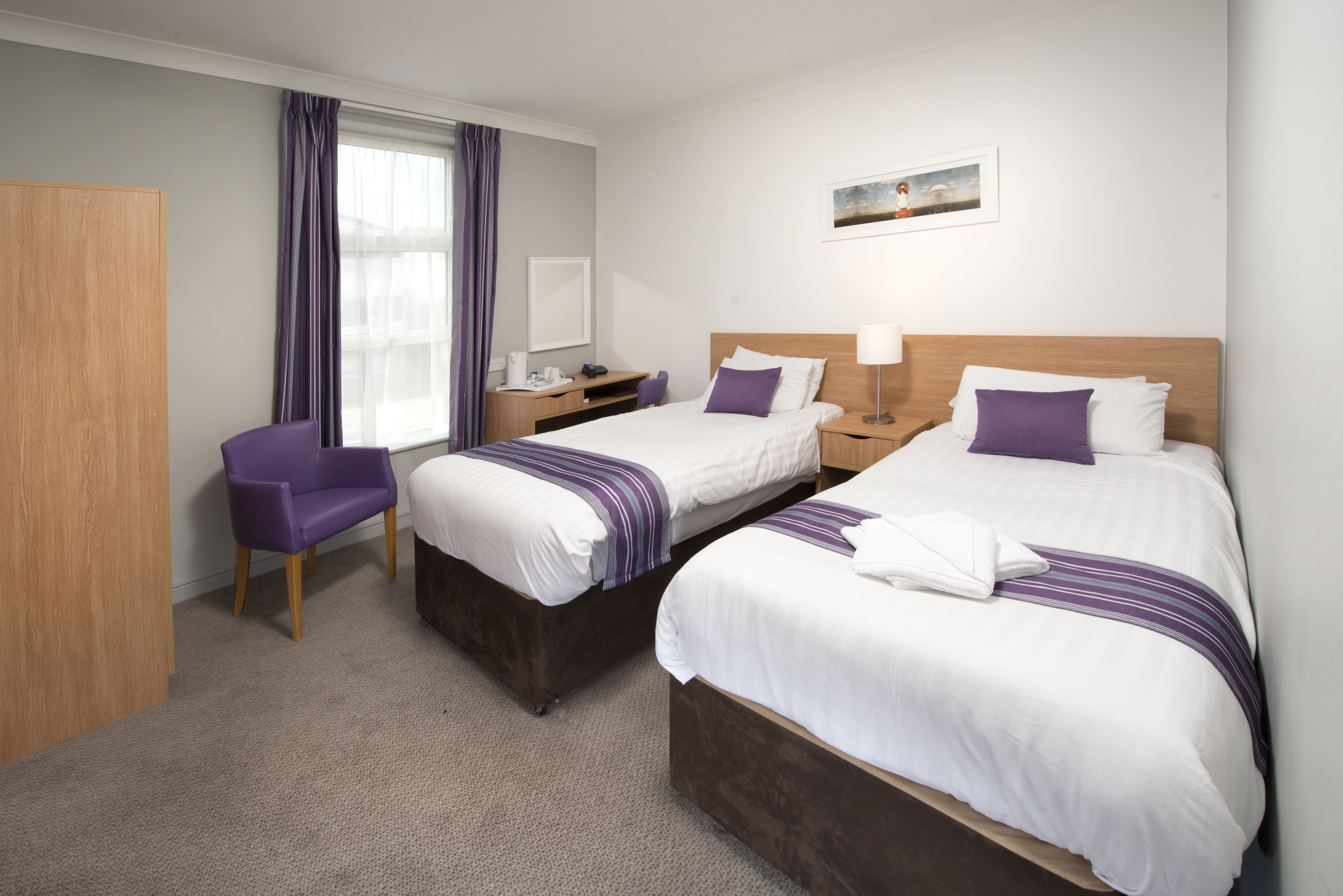 A hotel room with two beds, a desk, a chair, and a window with curtains.