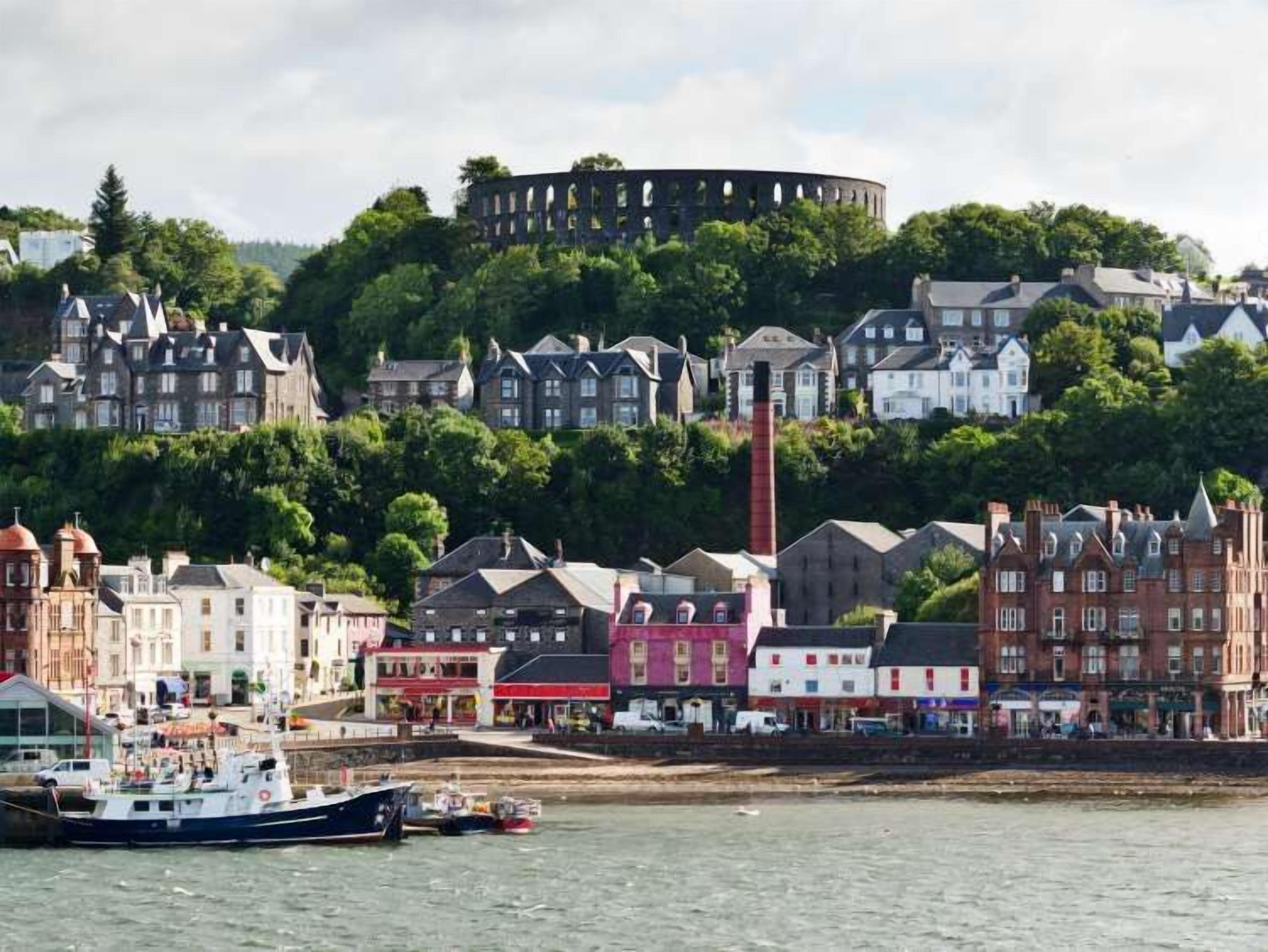 A coastal town with historic buildings, a prominent round tower, and a harbor with boats.