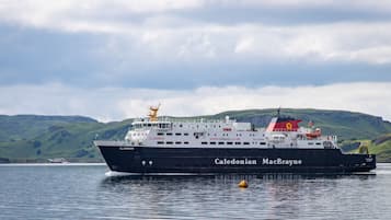 A large ship named Caledonian MacBrayne traveling on a body of water with green hills in the background.