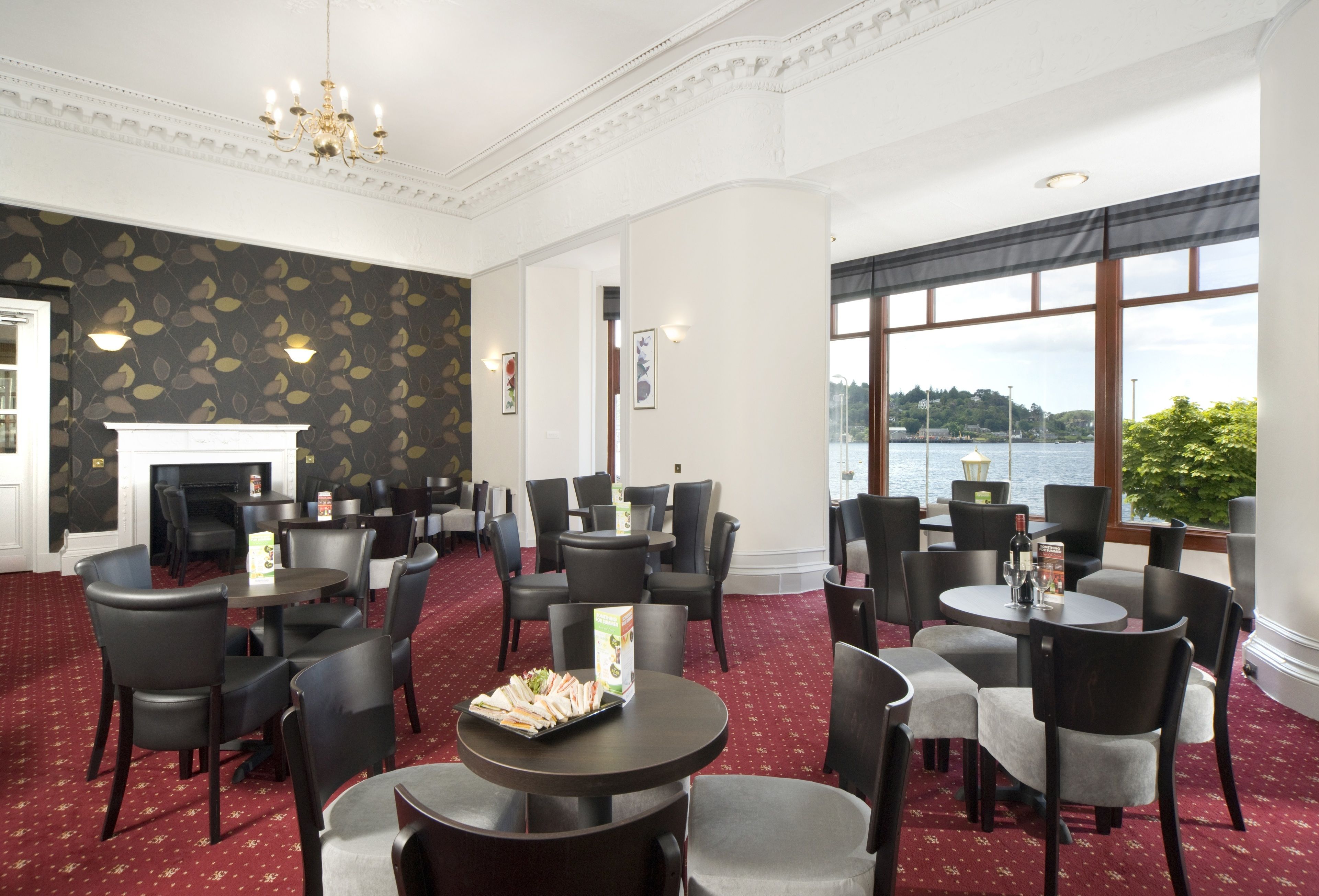 A hotel dining area with round tables and chairs, a fireplace, and a view of the water.