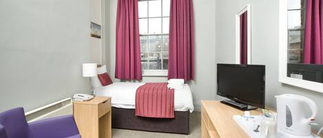 Habitación de hotel con cama, escritorio con hervidor, silla, televisión y ventana con cortinas.