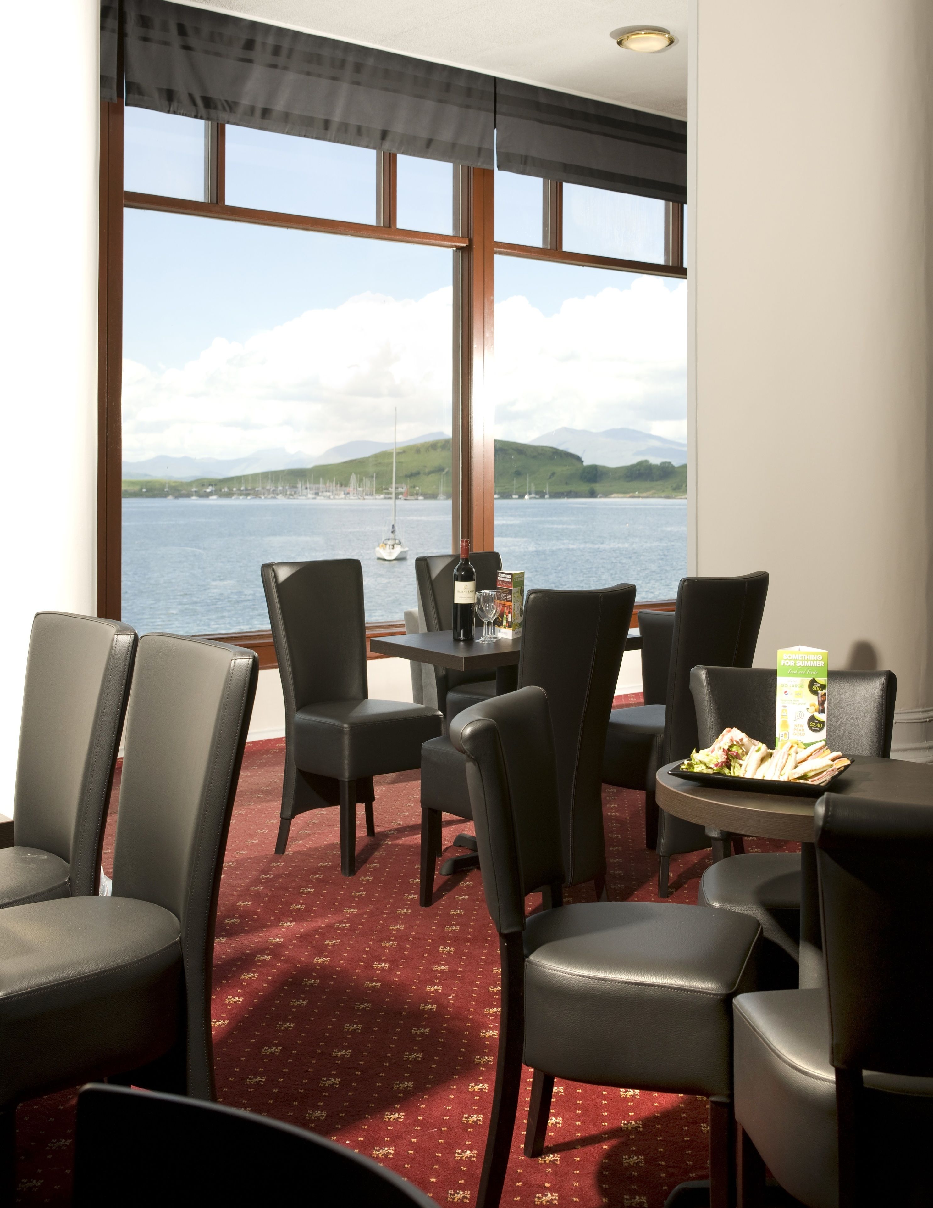 A room with a view of a body of water, a table with a bottle and a menu, and several chairs.