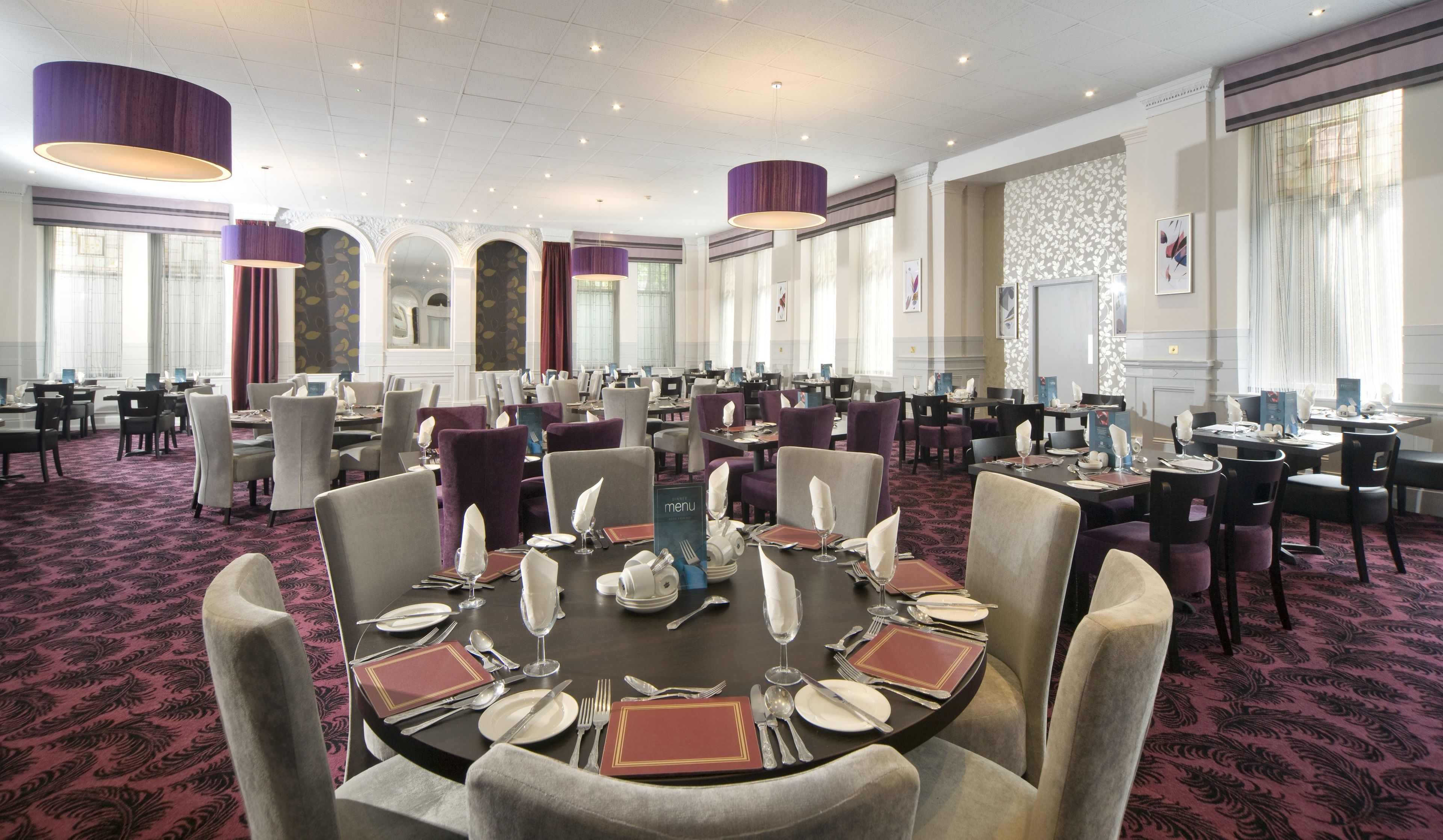 A large banquet hall with round tables set for dining, featuring a classic design with chandeliers and patterned carpet.