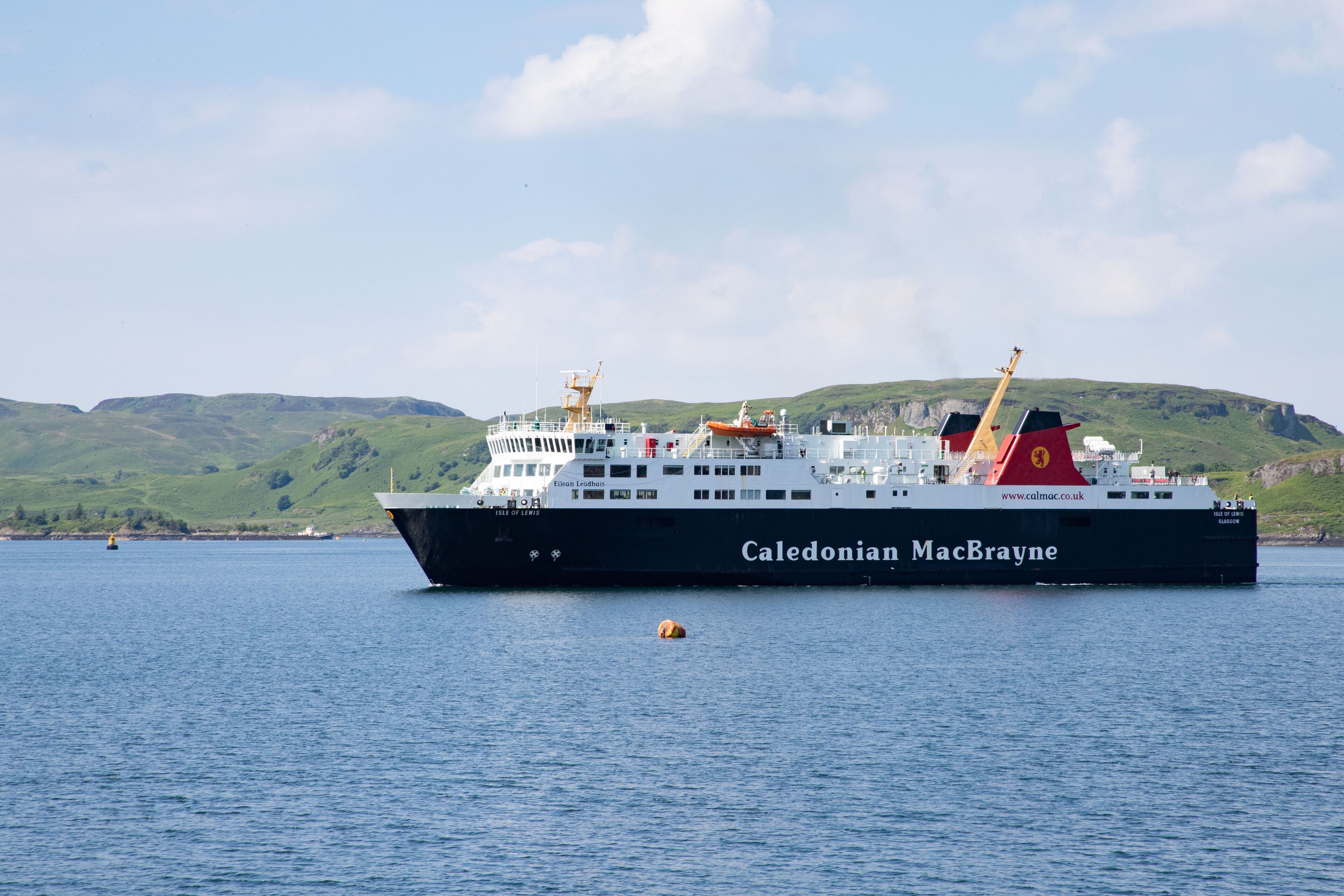 A large ferry named Caledonian MacBrayne traveling on a body of water with hills in the background.