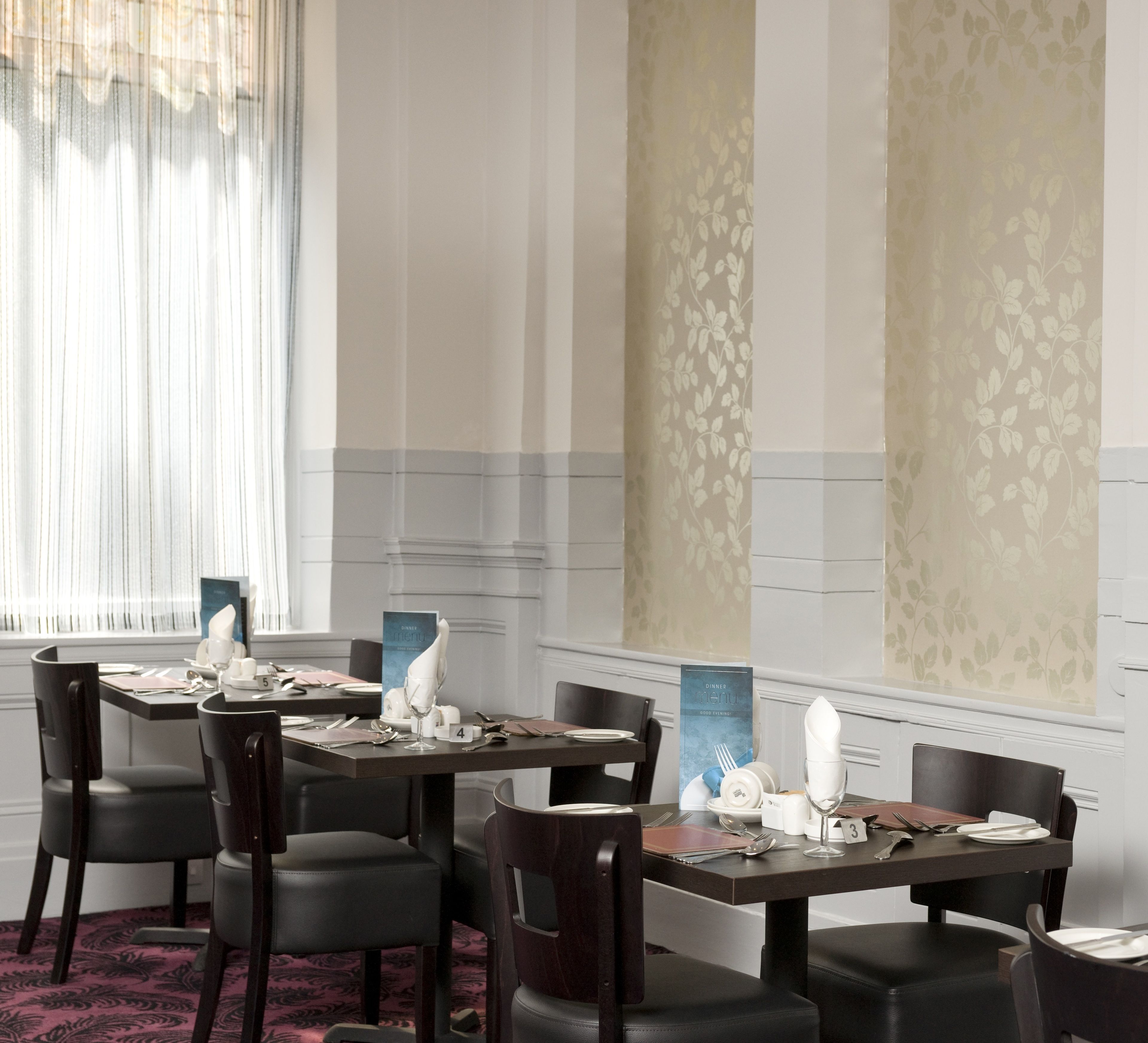 A dining area with tables set for four, each with a menu stand, plates, glasses, and cutlery.