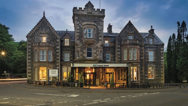 A historic stone building with a castle-like facade, a sign reading "Tarbet Hotel," and outdoor seating. - The Tarbet Hotel (Arrochar)