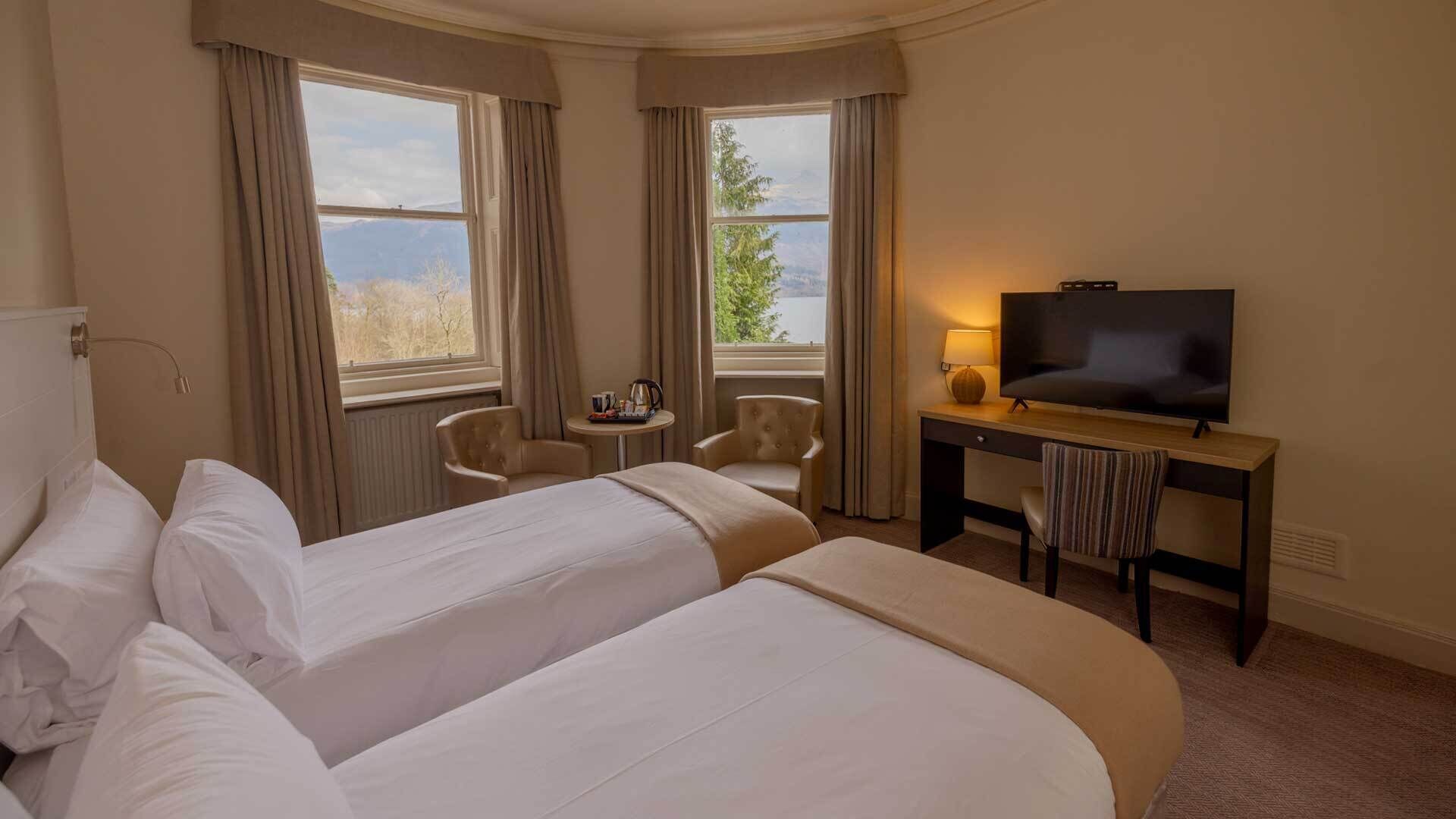 A hotel room with two beds, a desk with a TV, a chair, and a view of the outdoors.