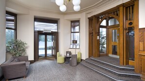 A lobby with a grey carpet, a brown sofa, a green armchair, a small table, and a staircase leading to an elevator. - The Tarbet Hotel (Arrochar)