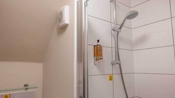 A shower with a handheld showerhead, a wall-mounted heater, and a soap dispenser.