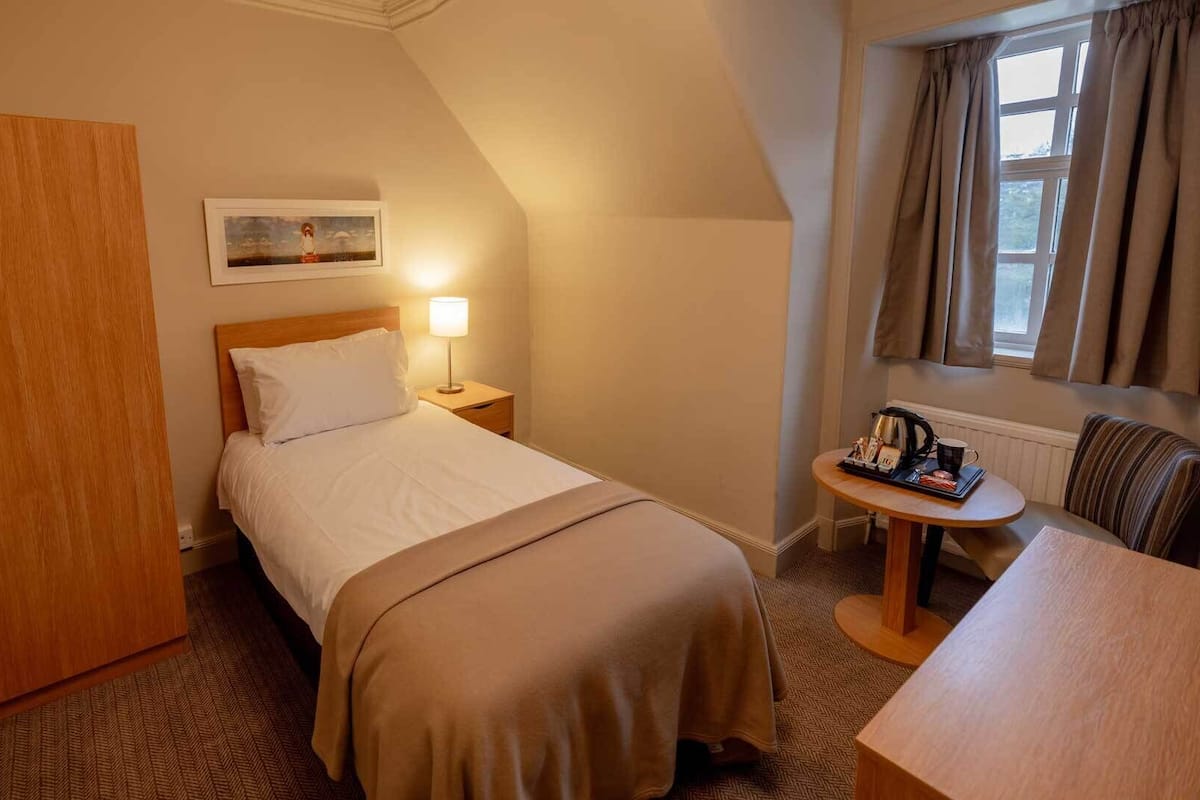 A hotel room with a bed, bedside table, lamp, and a small table with a coffee maker.