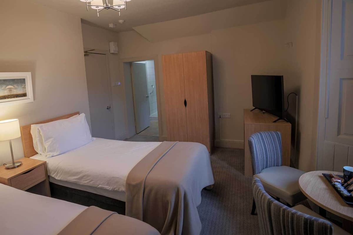 A hotel room with two beds, a desk with a chair, a television, and a painting on the wall.