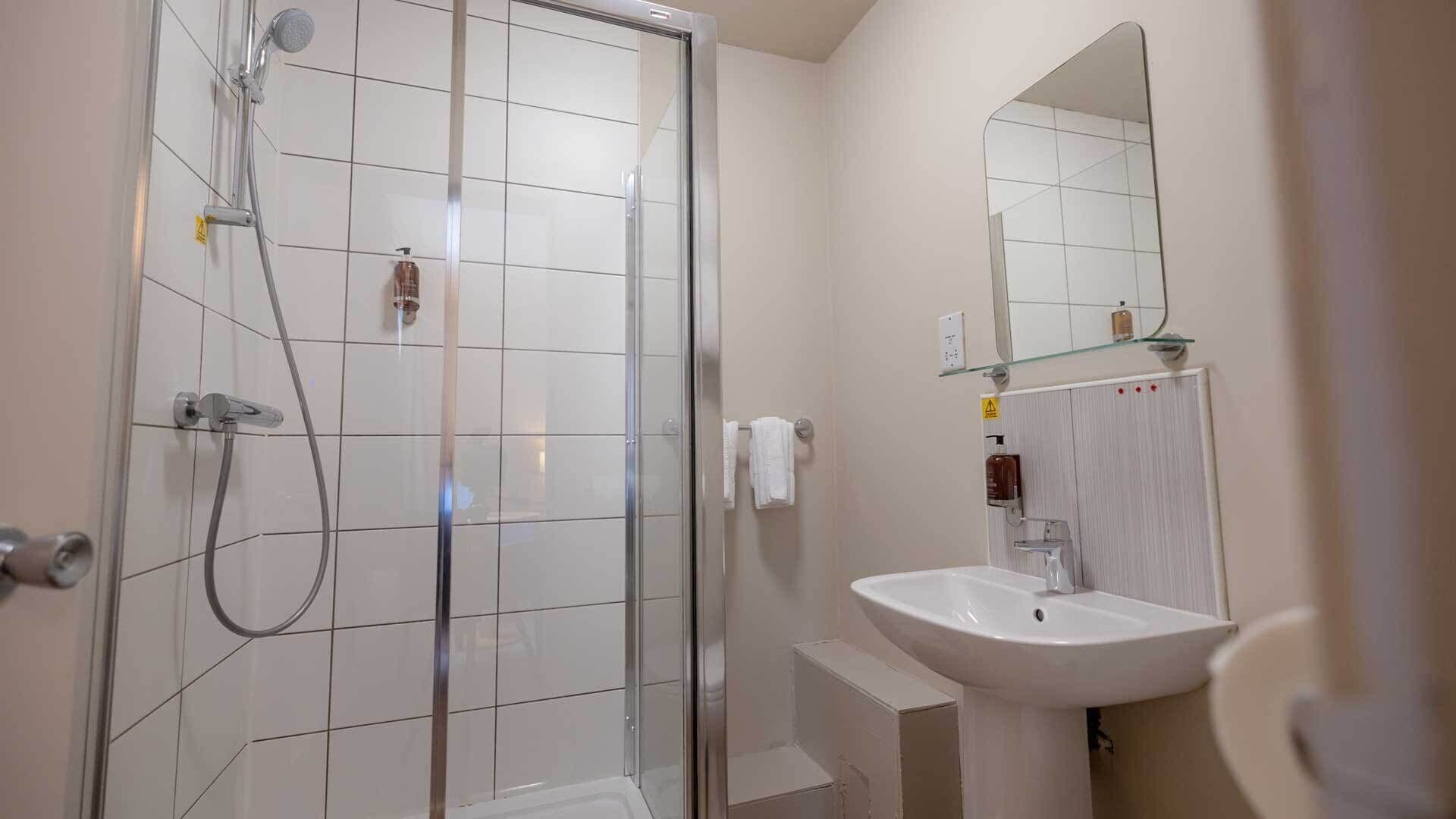 Een moderne badkamer met een glazen douchecabine, een witte wastafel en een spiegel boven de wastafel.