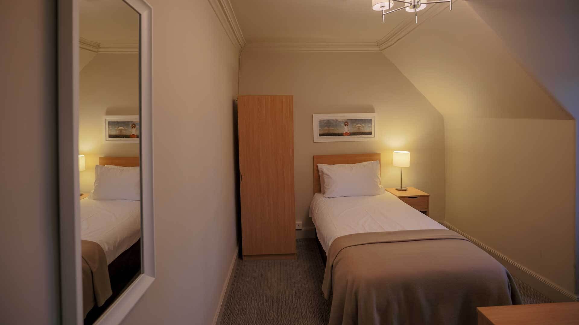A hotel room with two beds, a wooden wardrobe, a painting on the wall, and a mirror.