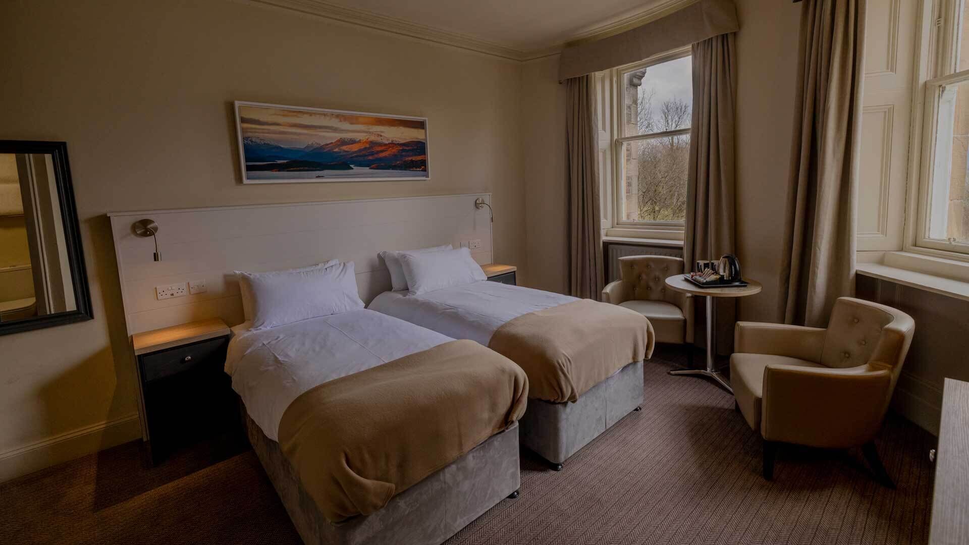 A hotel room with two beds, a small round table, a chair, and a painting on the wall.