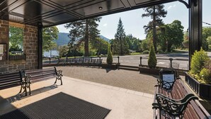 A covered outdoor seating area with benches and a view of a lake and mountains. - The Tarbet Hotel (Arrochar)