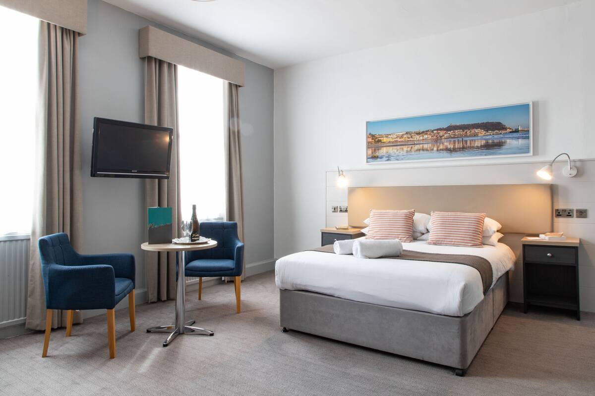 A hotel room with a bed, a TV, a desk, and a chair.