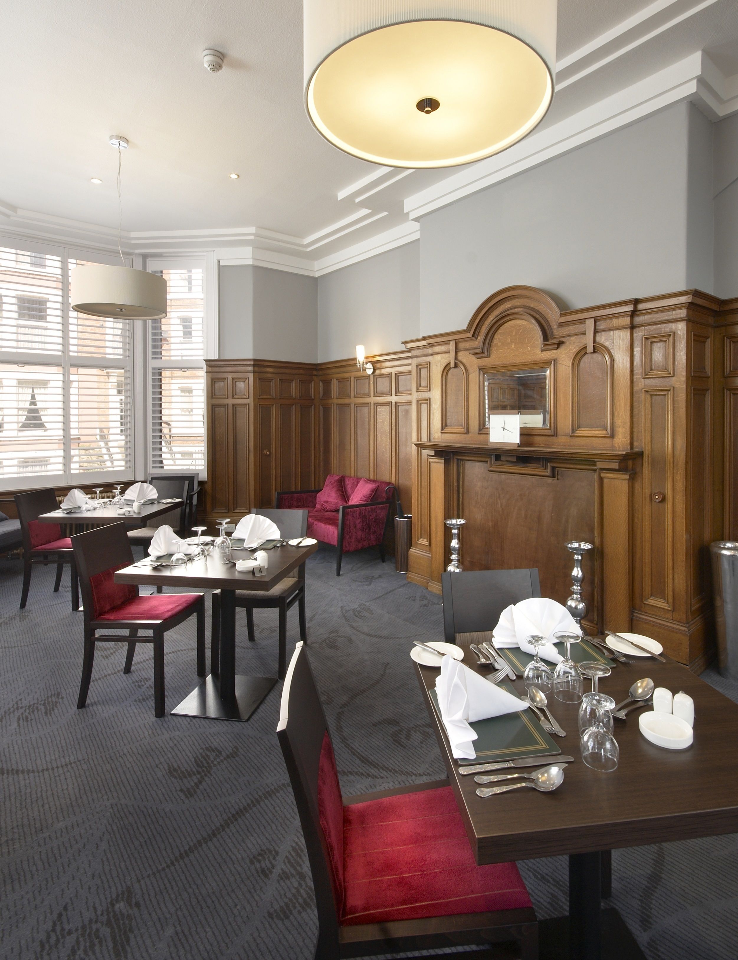 A hotel dining area with multiple tables set for dining, wooden paneling on the walls, and a large chandelier.