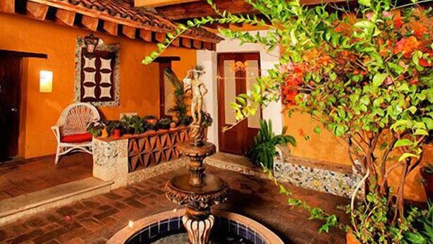 An outdoor courtyard with a fountain, potted plants, and a building with arches. - Hotel Azucena (Oaxaca)