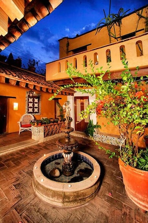 An outdoor courtyard with a fountain, potted plants, and a building with arches. - Hotel Azucena (Oaxaca)